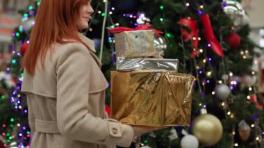 Kış tatili hazırlıkları, ellerinde hediyelerle aileye gülümseyen genç bir kadın gülümseyen ve perakende mağazasında süslenmiş Noel ağacının arka planındaki kameraya bakan.