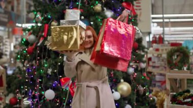 Ellerinde alışverişlerle mutlu bir kadın portresi, yeni yıl ağacının arka planındaki bir perakende mağazasında satıştan memnun.