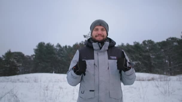 Retrato del hombre feliz en el bosque de invierno fondo de los árboles muestra clase, sonrisas y mira a la cámara — Vídeos de Stock