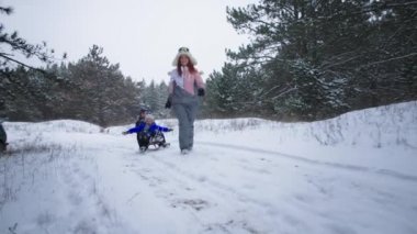 Aktif aile, mutlu anne kış tatilinde oğullarını karlı ormanda kızakla kayarken eğleniyor.