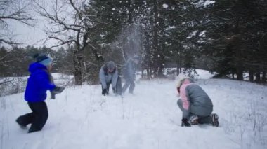 Kış aktiviteleri, mutlu aile küçük çocuklarla birlikte ormandaki ağaçların arka planındaki karların arasında kartopu oynarken iyi eğlenceler.