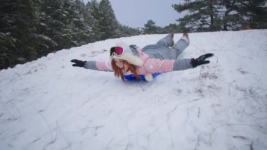 active winter vacation, happy woman slides down hill on sled while relaxing in a snowy forest