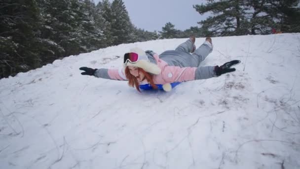 Active winter vacation, happy woman slides down hill on sled while relaxing in a snowy forest — Wideo stockowe