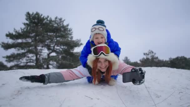 Outdoor activities, joyful mother with male child have fun sledding down snowy hill in forest on winter vacation — Stock Video