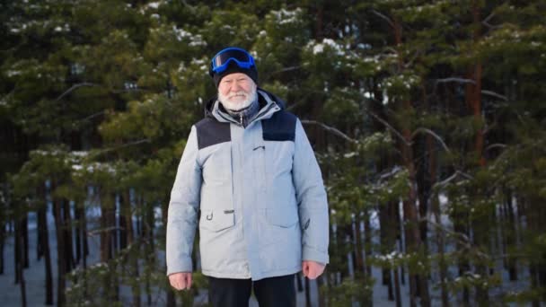 Portrét staršího muže v lyžařských brýlích a teplých šatech vede sportovní životní styl a radostně zvedá ruce při odpočinku v zimním lese mezi sněhem — Stock video