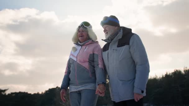 Starší pár, veselý starý manžel a manželka v lyžařských oddílech bavte se při procházce zimním lesem mezi sněhem a stromy za slunečného dne — Stock video