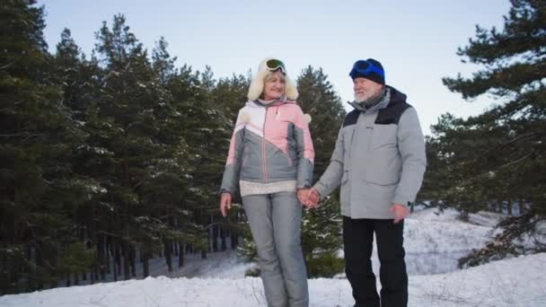 Active pensioners, charming elderly man and old woman have fun walking in winter in forest backdrop of snow and trees — Vídeo de Stock
