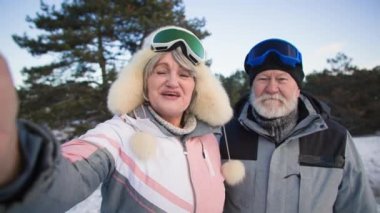 Emeklilikten sonra, modern yaşlı adam ve yaşlı kadın ormanda kar ve ağaçların arasında seyahat ederken arkadaşlarıyla cep telefonuyla video aracılığıyla iletişim kuruyor.
