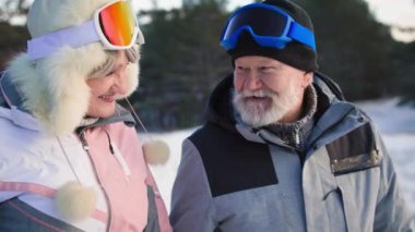Emeklilerin ilişkisi, spor giyim ve kayak gözlüklü neşeli yaşlı çift kar ve ağaçların arasında ormanda yürürken ortak tatilin tadını çıkarıyor.
