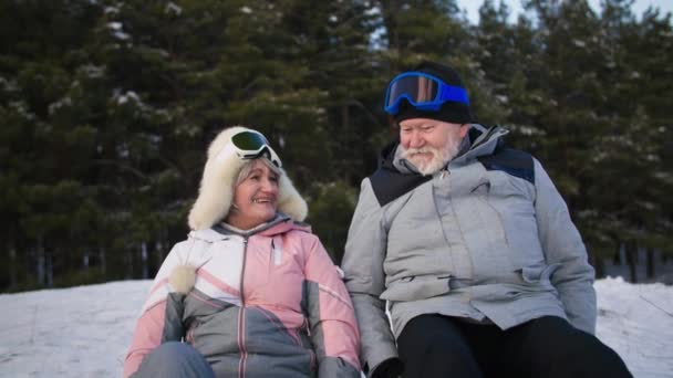 Lifestyle, active old husband and wife have fun in retirement sledding down a snowy slope in a winter forest strand of trees — Vídeo de Stock