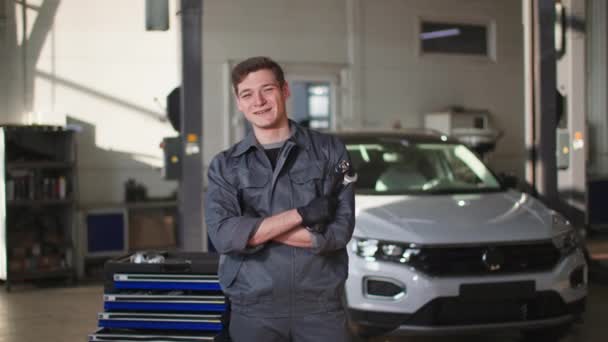 Portrait of a happy young man in uniform with tools in his hands working in a car service as a mechanic, smiling and looking at the camera — Vídeos de Stock