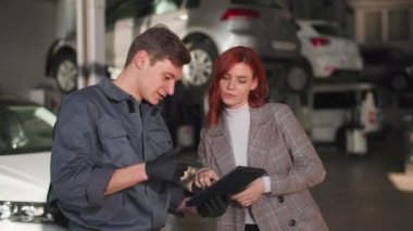 Araba servisi, genç bir erkek tamirci bayan bir müşteriyle konuşuyor ve tablette arabanın teknik durumunu gösteriyor.