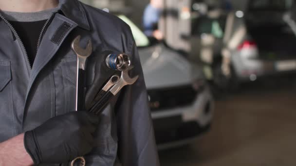 Serviço de carro, jovem um homem de uniforme fica com chaves ajustáveis em suas mãos em uma estação de serviço, close-up — Vídeo de Stock