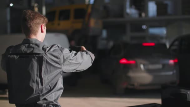 Young male mechanic in uniform regulates movement of a car during a check-in at a site for technical inspection in a car service, rear view — Stok video