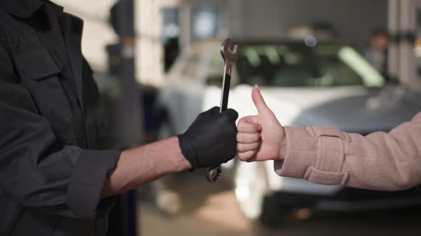 Jistota, automechanik s klíčem v ruce zvedne ruku spolu se spokojenou kolegyní, ukazuje palec nahoru, dobrý servisní koncept, detailní záběr — Stock video