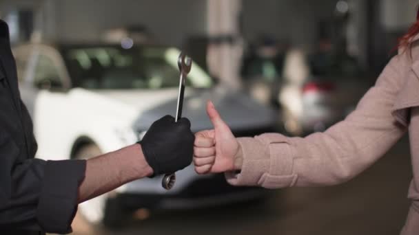 Bil service, nöjd kvinnlig kund visar tummen upp tillsammans med manlig mekaniker med skiftnyckel i händerna, närbild — Stockvideo