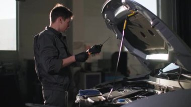 Profesyonel erkek tamirci, teknik bir istasyonda yeni bir arabanın motorunda yağ seviyesini kontrol ediyor.