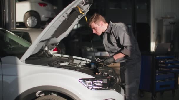 Mecânico masculino profissional em uniforme com ferramentas em suas mãos verifica o estado de um motor de carro em uma estação técnica — Vídeo de Stock