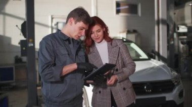 Otomobil işi, çekici kız ve tabletli teknisyen portresi benzin istasyonunda araba bakımı hakkında konuşuyor.