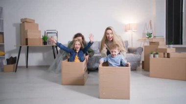 Küçük şirin çocukları olan karton kutularla koşan mutlu genç ebeveynler. Aile sahipleri, taşınma günü eğleniyor.