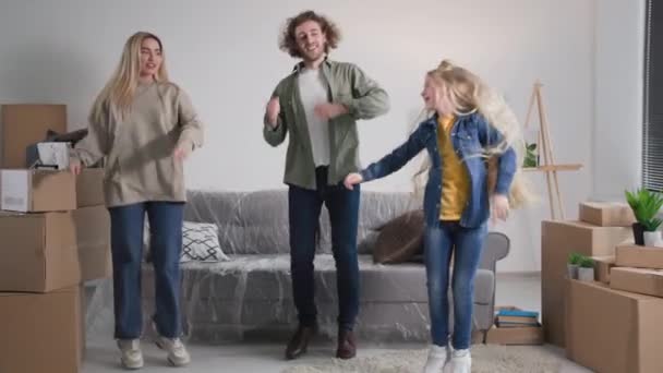 妈妈爸爸和女儿在搬家的那天一起跳舞很开心 年轻的家庭被纸板箱围绕着庆祝买房子或公寓 — 图库视频影像