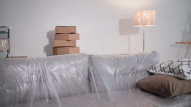 Taşındıktan sonra oda, plastik ambalajla kaplı mobilyalar ve boş bir dairede bir sürü karton kutu, kamera hareket halinde.