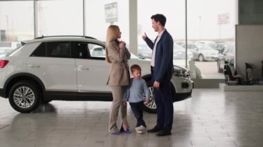 Aile arabası almak, neşeli genç bir çift ve küçük bir çocuk yeni bir araba almaktan mutlular, şov anahtarları, gülümseme ve kameraya bak.
