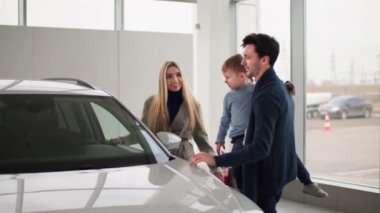 Aile arabası satın alma, mutlu bir eş, kollarında kocası ve oğluyla birlikte, araba galerisinden yeni bir aile arabası modeli seç.