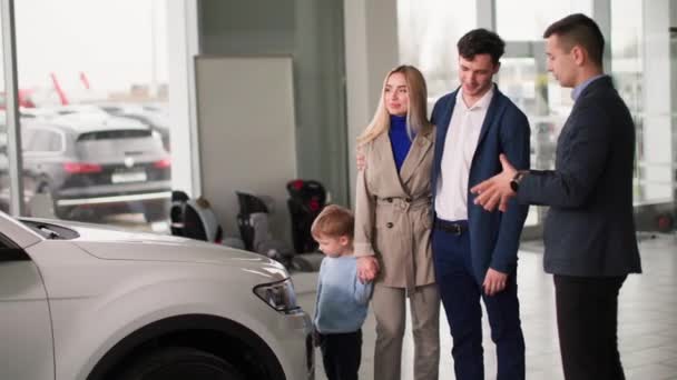 小さな男の子を持つ車のディーラー 喜びの男と女性はディーラーで家族の自動車を選択し セールスセンターのマネージャーと相談します — ストック動画