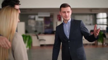 Otomobil satış merkezi, genç profesyonel erkek müdür araba galerisindeki yeni arabaları erkek ve kadın alıcılara anlatıyor.