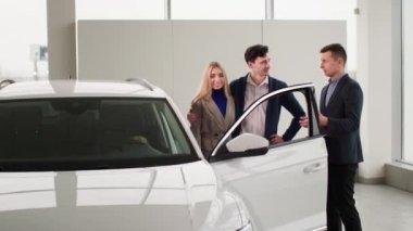 Aile alıcıları yeni araba seçiyor, profesyonel pazarlamacı erkek danışman otomobil satış merkezinde çocuklu evli çifte yeni otomobil modeli hakkında konuşuyor.