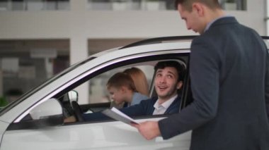 Araba alan, ailesi olan mutlu adam yeni araba direksiyonunda oturan ve otomobil satıcısıyla konuşan.