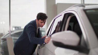 Otomobil merkezi, genç, neşeli erkek müşteri araba galerisinde keyfi olan yeni arabaya bakıyor.