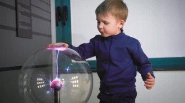 Sevimli küçük çocuk eliyle plazma topuna dokunuyor, elektrik dalgaları yaratıyor, etkileşimli oyuncaklar yaratıyor.