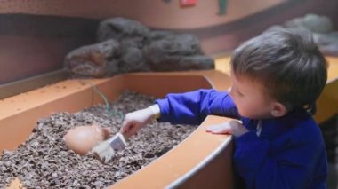 small male child playing with an archaeological excavation simulator, cleaning sand vase with brush in a museum