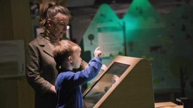 methods of educating children, loving mother helps her male child to be trained on touch monitor in the room