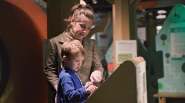 methods of educating children, woman helps her male kid to be trained on touch swipes across sensor monitor in indoors