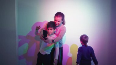 science and education, cheerful brothers pose for a photo on a smartphone background of mixed colors in science museum for children
