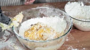 loving female ol parent teaches daughter how to make egg and wheat flour dough for baking, close-up