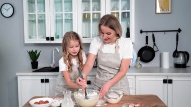 cooking together with a child, happy little girl together with her mother stirs dough from wheat flour