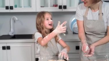 cooking training for child, beautiful little girl together with mother prepares wheat flour dough for making buns at home in kitchen