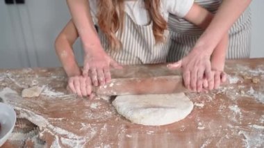 loving mother together with daughter preparing liver or gingerbread from wheat flour and rolling out dough together at table in kitchen at home, close-up