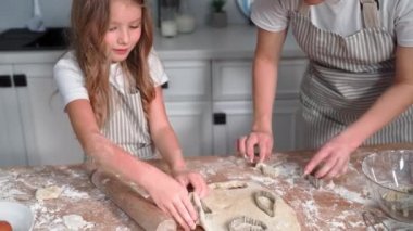 child learning to cook, adorable little girl together with mother make cookies from dough using baking molds on kitchen table at home