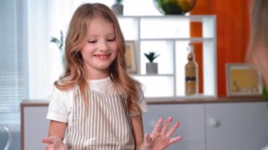 smiling little girl having fun together with mom preparing dough buns and giving five hands in flour at home in kitchen
