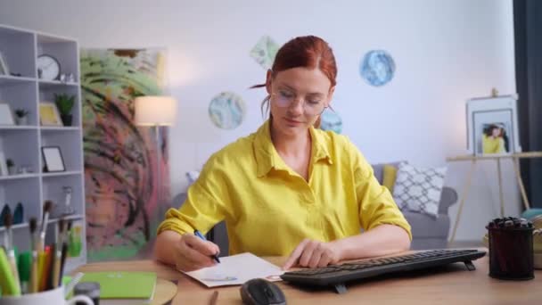 靴のデザイン 女性は現代のアパートのコンピュータに座っている間に紙に靴のプリントを描きます — ストック動画