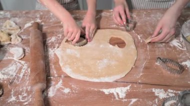 Ev yapımı kurabiyeler, gayretli bir kız ve anne birlikte zencefilli kurabiye pişirip mutfak masasındaki hamurdan ekmek kalıbı kullanarak simit kesiyorlar.