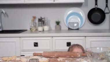 Bayan çocuk buğday unundan zencefilli ekmek pişirirken ve masanın altından gözetlerken eğleniyor.