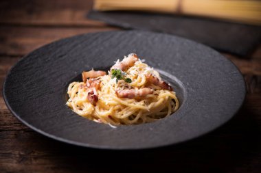 Siyah tabakta, beyaz ahşap bir masada, Carbonara makarnası.