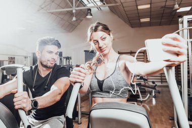 Spor salonunda selfie çeken gülümseyen bir çift. Spor giyimli genç erkek ve kadınlar spor salonunda selfie çekiyorlar. Kapat şunu.