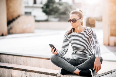 Genç ve mutlu bir kız şehirde akıllı telefon kullanıyor.
